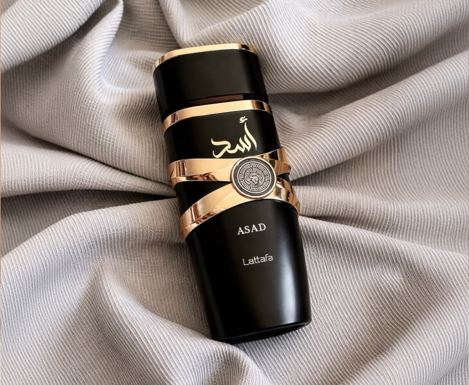 Parfum Asad de Lattafa, flacon noir et or posé sur un tissu gris